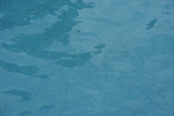 Blue swimming pool water surface with gentle ripples and sunlight reflections. Calm aqua texture creating a refreshing and relaxing summer atmosphere. Perfect background for vacation, spa, and wellnes