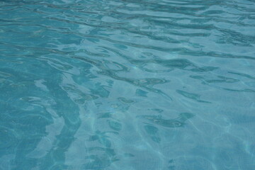 Blue swimming pool water surface with gentle ripples and sunlight reflections. Calm aqua texture creating a refreshing and relaxing summer atmosphere. Perfect background for vacation, spa, and wellnes