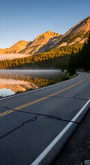 Scenic mountain road winding alongside a misty lake reflecting sunlit peaks and evergreen forest