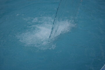 Stream of clear water flowing into a blue swimming pool. Freshness, purity, and relaxation concept for spa, resort, or wellness design.