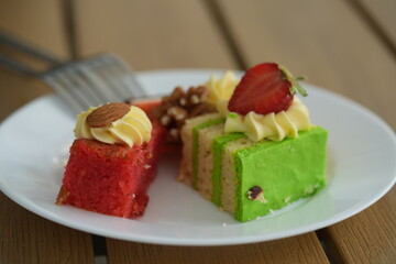 Elegant dessert assortment with colorful cakes, strawberry topping, and cream decoration served on a white plate. Perfect image for hotels, restaurants, catering companies, and bakery brands promoting