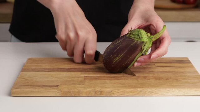 hands slicing organic eggplant on cutting board cooking food