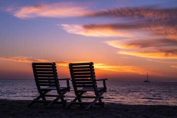 Serene Sunset Scene: Two wooden beach chairs sit on the beach, offering a serene view of a beautiful sunset, as gentle waves lap the shore creating a tranquil atmosphere.