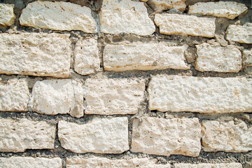 Textured wall of rectangular stone blocks in light beige shades and cement between them.