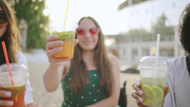 three female multiracial friends one disabled woman in a wheelchair celebrate together by raising colorful drinks under the sun at a lively outdoor cafe on a warm day - Powered by Adobe