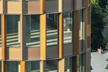 Modern residential or office building with golden facade and glass windows overlooking green trees and suburban houses in the city of Vilnius
