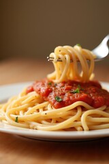 A close-up of spaghetti on a white plate with tomato sauce and herbs. The background is blurred with soft warm lighting