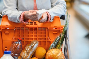 The hands of an elderly woman hold a receipt for groceries in a supermarket. The concept of high...