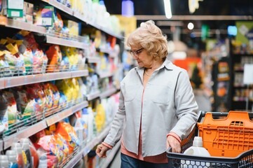 Elderly woman buying household chemicals or laundry detergent at supermarket.