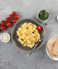 Scrambled eggs with microgreens, tomatoes, toast on grey background. Healthy breakfast. Top view.