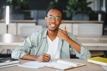 Obraz premium Smiling young man studying and showing thumbs up in library