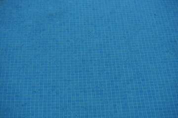 Blue swimming pool with visible square tiles under the water. Clear aqua surface creates a refreshing summer holiday background.