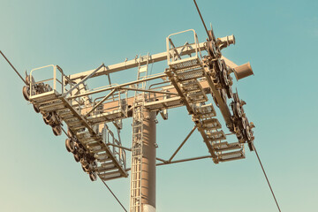 Close up of a cable car support pylon featuring maintenance platforms and wheels, set against a clear blue sky © EdNurg