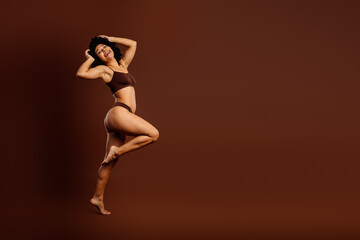 Beautiful young woman posing in stylish brown lingerie against elegant monochromatic background,...