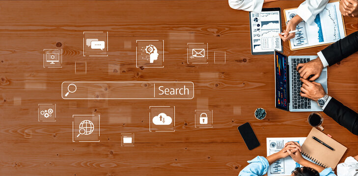 A dynamic office meeting scene showcasing collaboration among professionals, featuring laptops, data analytics, charts, and a digital search interface on a wooden table. Trope - Powered by Adobe
