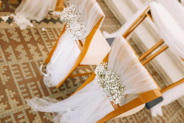 Elegant church wedding ceremony decoration with chairs adorned with white fabric, flowers, and ribbons, creating a romantic and festive atmosphere for the bride and groom