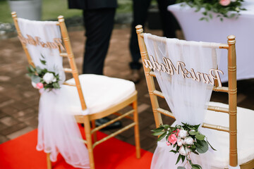 Elegant church wedding ceremony decoration with chairs adorned with white fabric, flowers, and ribbons, creating a romantic and festive atmosphere for the bride and groom