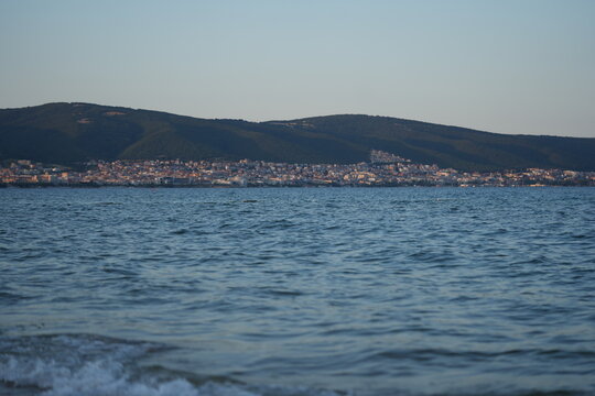 Coastal city view across the blue sea with distant hills and skyline. Tranquil seascape with calm waves, clear sky, and seaside architecture — perfect for travel, tourism, or nature backgrounds. - Powered by Adobe