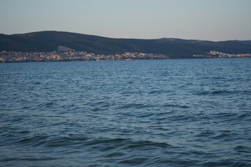 Coastal city view across the blue sea with distant hills and skyline. Tranquil seascape with calm waves, clear sky, and seaside architecture — perfect for travel, tourism, or nature backgrounds.