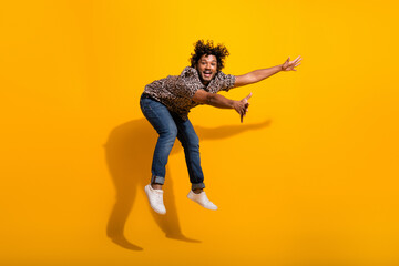 Energetic young man in a leopard print shirt jumps playfully against a vibrant yellow background, showcasing fashion and enthusiasm