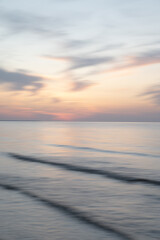 A dreamy, impressionistic paint like blurred sea sunset background with gently soft pastel colours. Vertical photo.