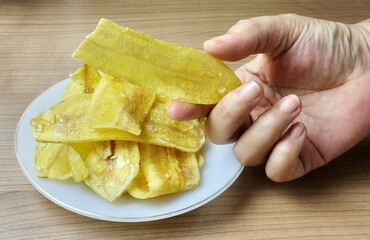 A hand holds delicious golden crispy banana chips, a popular Thai native souvenir snack from local farmer groups, crunchy and sweetly addictive.