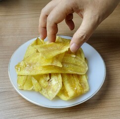A hand holds a crispy golden banana snack, famous throughout Thailand. It's made from thinly sliced fried bananas coated in a delicious sugar glaze.