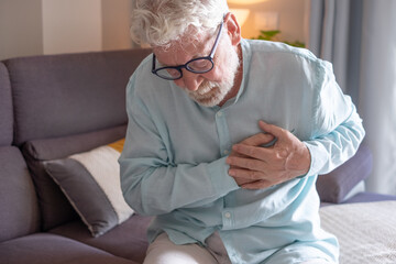 Senior man experiencing chest pain at home, holding his chest with a distressed expression. Concept...