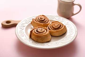 Plate with tasty cinnamon rolls on pink background