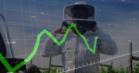Adjusting VR headset, man in protective coat viewing green line chart overlay over vineyard rows