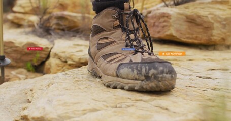 Resting brown hiking boot displaying mud-covered sole on sandstone boulder, with trekking pole