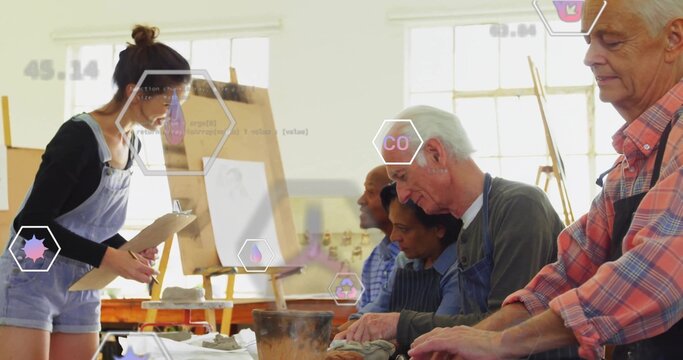 Instructor coaching students wearing aprons shaping clay on bench at pottery studio, with tablet
