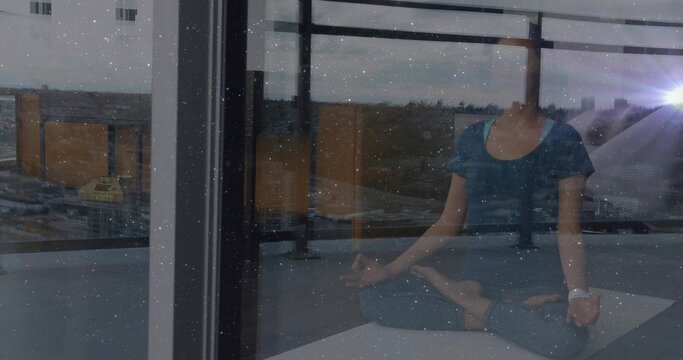 Meditating woman wearing teal outfit, smartwatch on yoga mat on balcony by glass panels, copy space - Powered by Adobe
