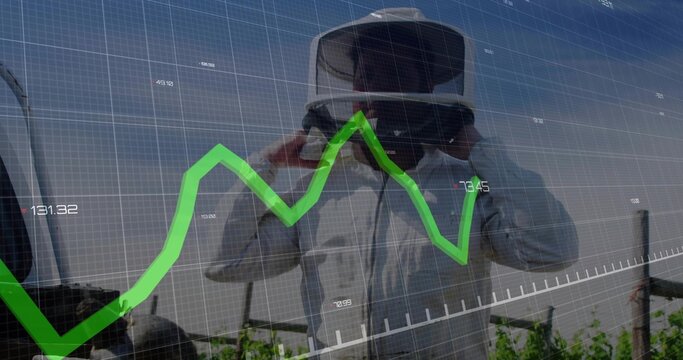 Adjusting VR headset, man in protective coat viewing green line chart overlay over vineyard rows
