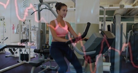 Pedaling woman wearing pink sportswear on exercise bike in gym, with heart-rate graph overlay