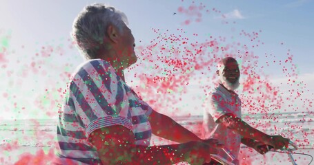 Pedaling senior couple wearing striped shirt and polo shirt on seaside bike path, with bicycles