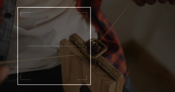 Craftsman in plaid shirt securing brass belt buckle and threading strap through clamp on workbench