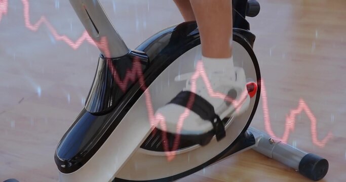 Fototapeta Pressing black-and-white sports shoe onto exercise bike pedal in home gym, red line graph overlay