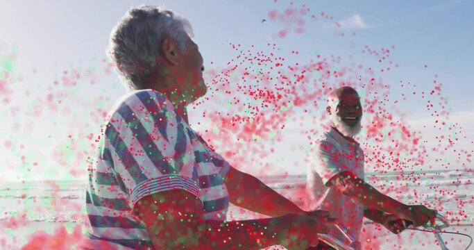 Pedaling senior couple wearing striped shirt and polo shirt on seaside bike path, with bicycles