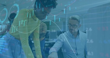 Pointing colleague in green turtleneck reviewing charts in open-plan office, with computer monitors