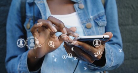 Tapping smartphone woman wearing denim jacket and white tank scrolling user icons at urban wall