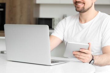 Male teacher with laptop and tablet computer giving online lesson at home, closeup