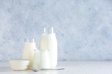 Bottles and glass bowl of tasty yogurt on white background