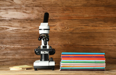 Modern microscope with copybooks and sticky notes on table against wooden background