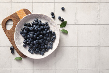 Wooden cutting board and plate with fresh ripe blueberry on tile background