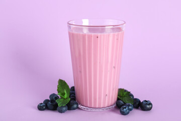 Glass of fresh blueberry smoothie with mint and berries on lilac background