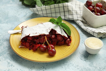 Plate with piece of tasty cherry strudel and napkin on blue grunge background