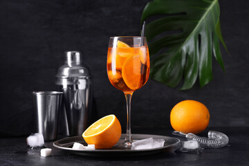 Glass of Aperol spritz cocktail with shaker and palm leaf on black background