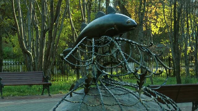 Copper statue depicting caught in the nets of cod in autumn the park.
