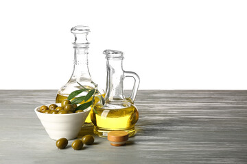 Decanters of fresh olive oil on grey wooden table against white background